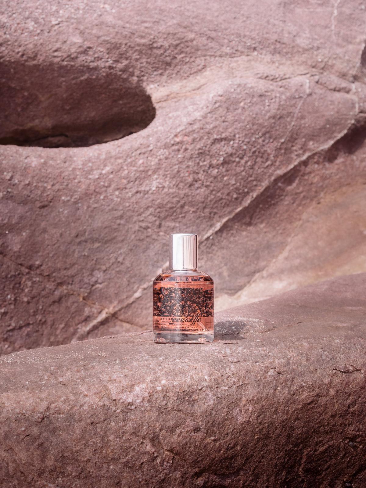 Flacon du parfum Leenaëlle d’Opposée posé sur une roche dans une lumière douce.
