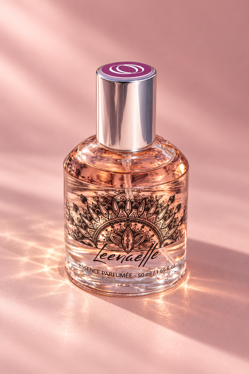 Flacon de parfum Leenaëlle 50 ml en verre transparent, décoré d’un motif floral noir et fermé par un capuchon argenté, sur fond rose poudré avec des reflets lumineux et une ombre douce.