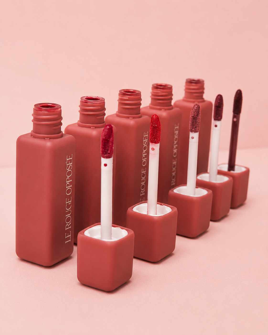 Les cinq teintes du Rouge Opposée avec leurs applicateurs sur fond rose