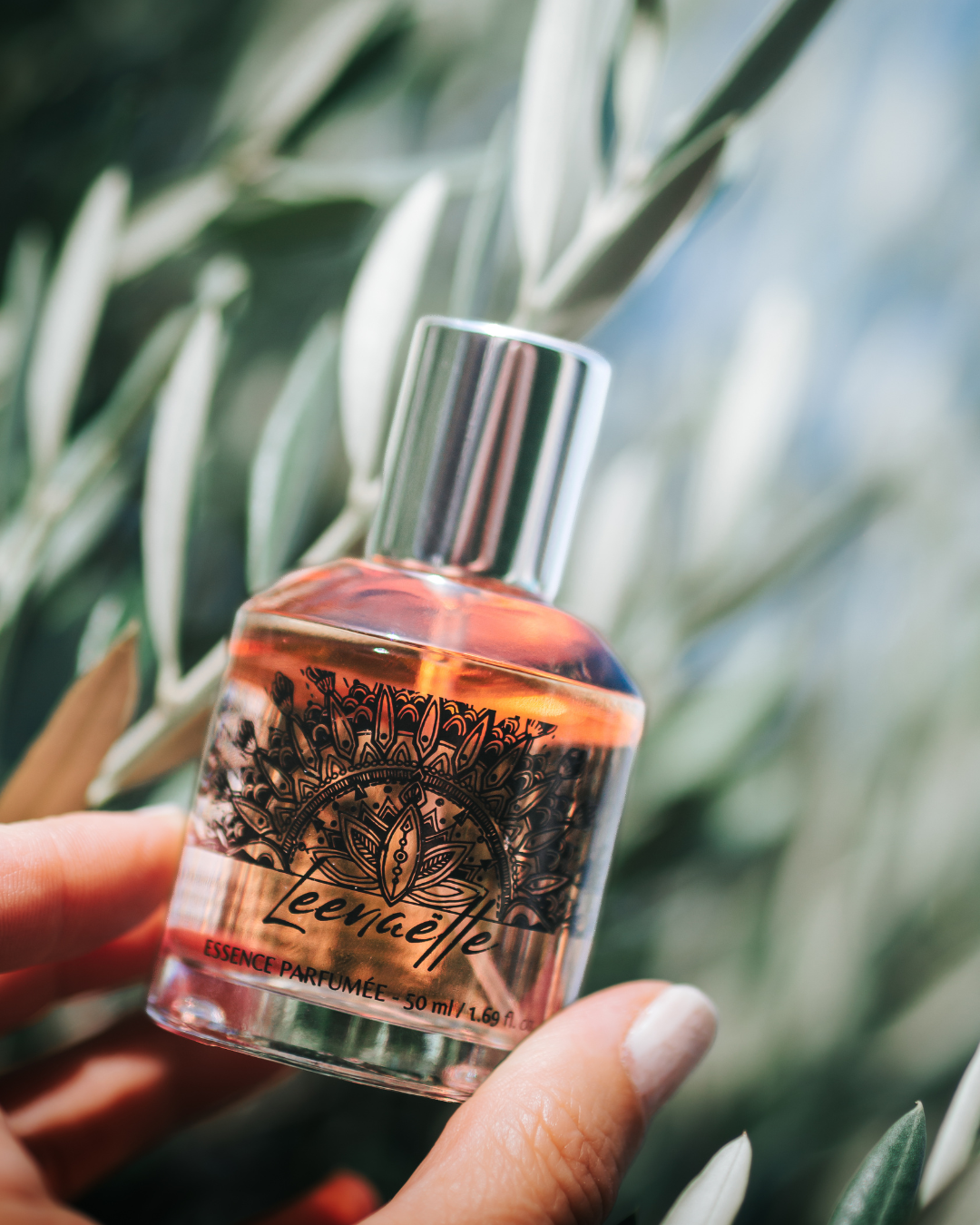 Flacon Leenaëlle 50 ml tenu à la main devant une végétation baignée de lumière.