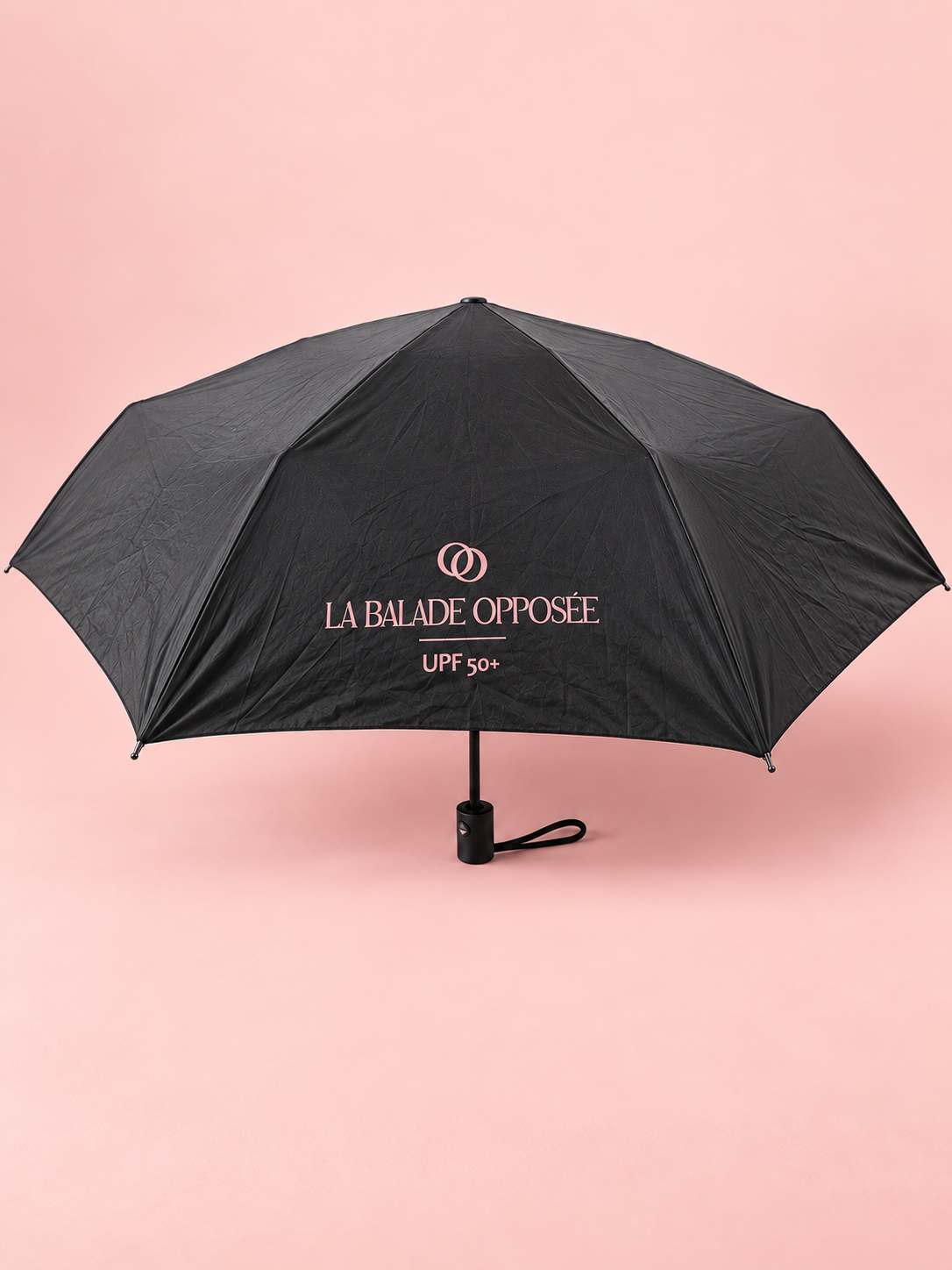 Parapluie pliable noir anti-UV UPF 50+ La Balade Opposée ouvert sur fond rose poudré