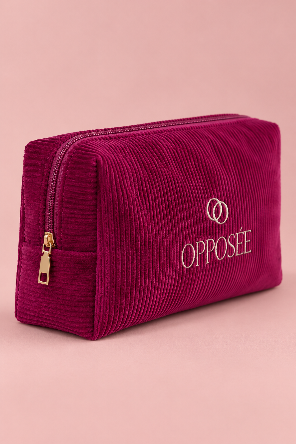 Trousse de maquillage Opposée en velours côtelé bordeaux rosé, fermée sur fond rose poudré.