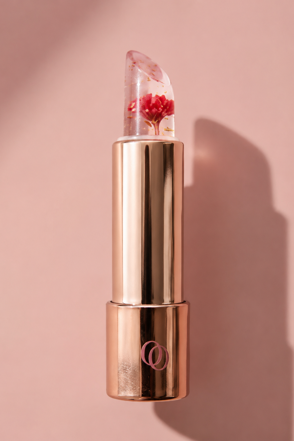 Caresse Opposée, baume à lèvres rose gold transparent avec fleur intégrée, sur fond rose.